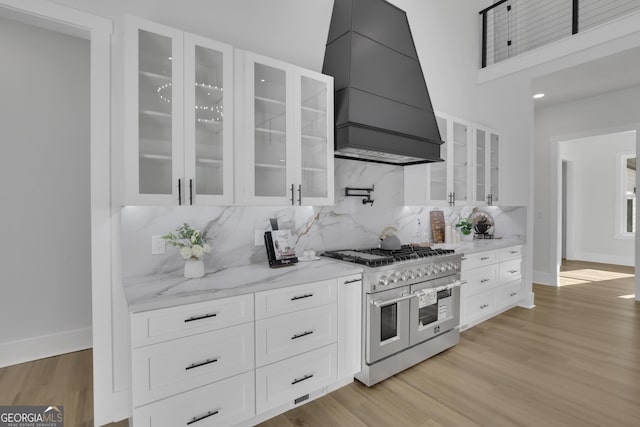 kitchen with backsplash, range with two ovens, custom range hood, white cabinets, and light stone counters