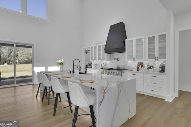 kitchen featuring light stone countertops, a high ceiling, custom exhaust hood, white cabinetry, and stove