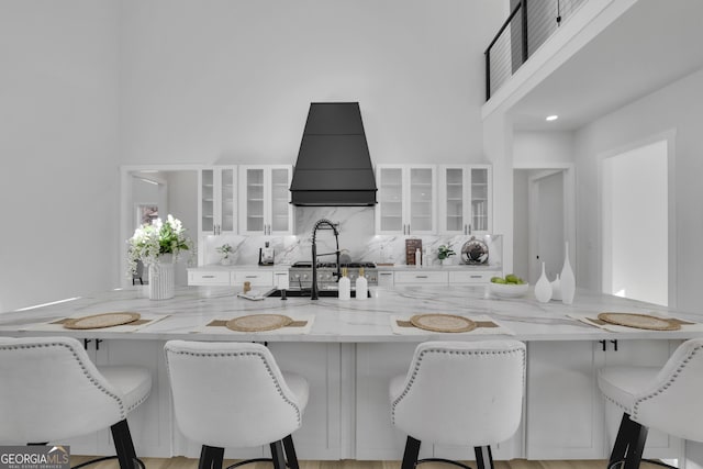 kitchen with a kitchen bar, light stone counters, white cabinetry, and custom range hood