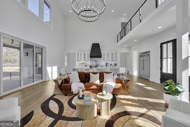 living room with a towering ceiling, sink, an inviting chandelier, and light hardwood / wood-style flooring