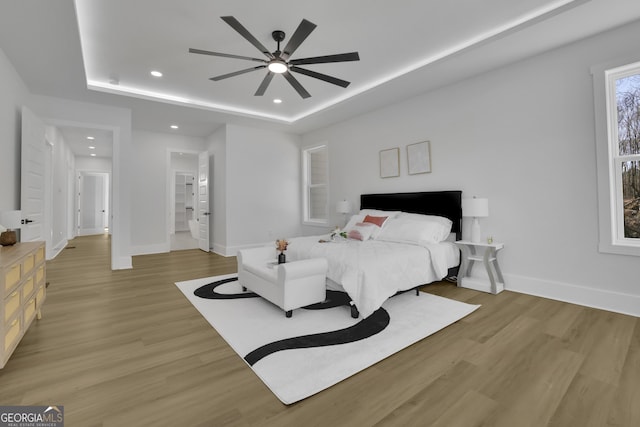 bedroom featuring ceiling fan, a tray ceiling, and light hardwood / wood-style floors