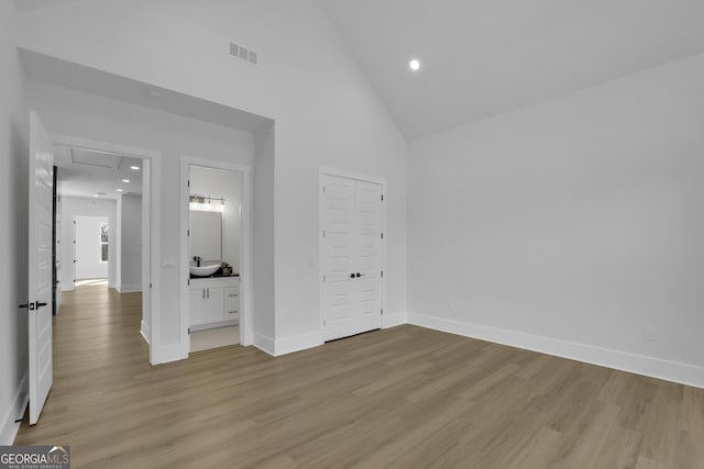 unfurnished bedroom with ensuite bathroom, sink, light wood-type flooring, high vaulted ceiling, and a closet