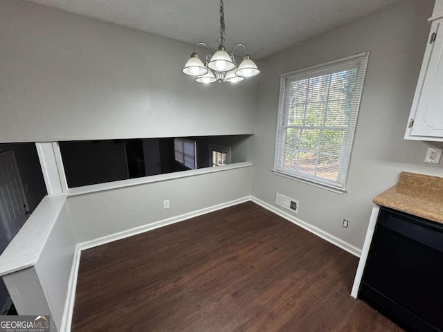 unfurnished dining area with dark wood-type flooring, a chandelier, and a textured ceiling