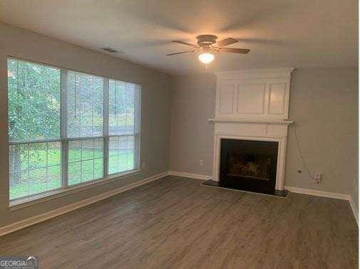 unfurnished living room featuring ceiling fan, a large fireplace, dark hardwood / wood-style floors, and a healthy amount of sunlight