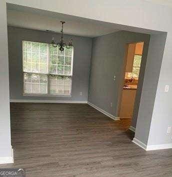 unfurnished dining area featuring dark wood-type flooring and an inviting chandelier