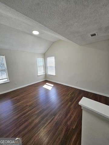 unfurnished room featuring a textured ceiling, dark wood-type flooring, and lofted ceiling