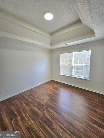 unfurnished room with a textured ceiling, dark wood-type flooring, and a tray ceiling