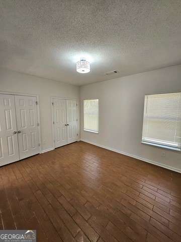 unfurnished bedroom featuring a textured ceiling, two closets, and dark hardwood / wood-style floors