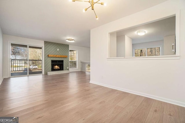 unfurnished living room with a large fireplace, light hardwood / wood-style flooring, and a notable chandelier