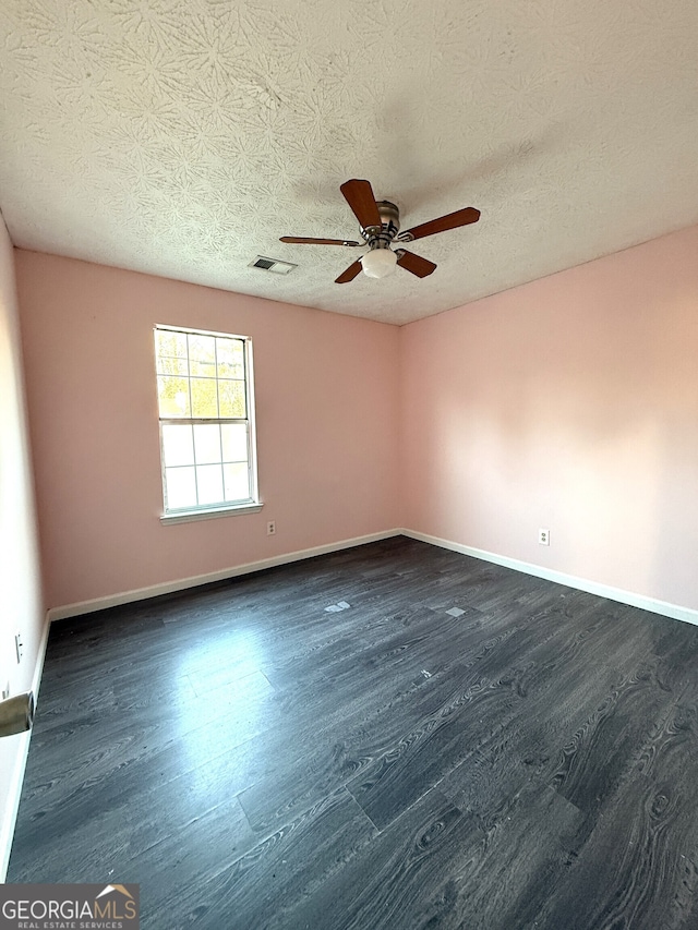 empty room with ceiling fan, dark wood-type flooring, and a textured ceiling