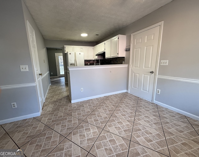 kitchen featuring backsplash, kitchen peninsula, white cabinetry, white refrigerator with ice dispenser, and a textured ceiling