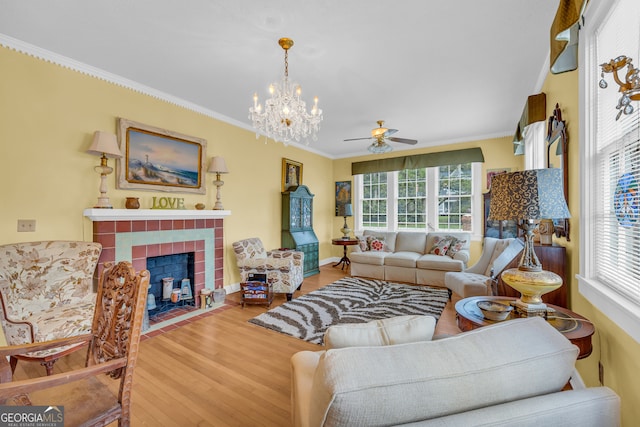 living room with hardwood / wood-style flooring, ornamental molding, ceiling fan with notable chandelier, and a fireplace