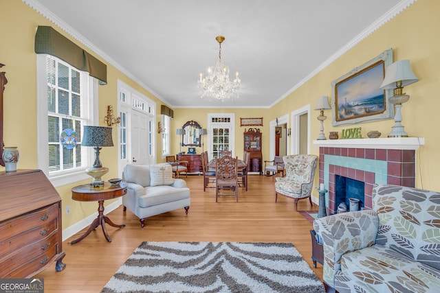 living area with hardwood / wood-style flooring, ornamental molding, a chandelier, and a tiled fireplace