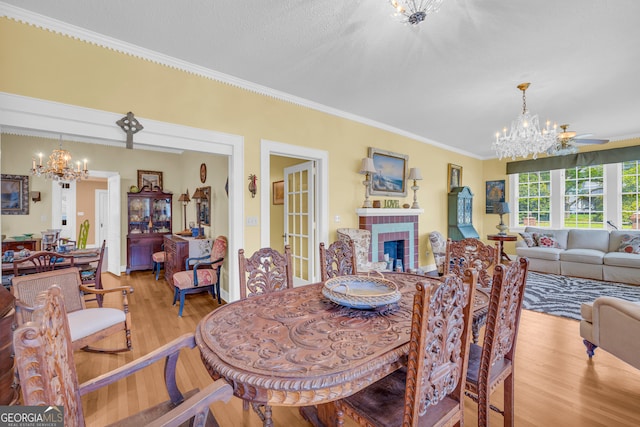 dining space with a tile fireplace, a notable chandelier, a textured ceiling, ornamental molding, and light wood-type flooring