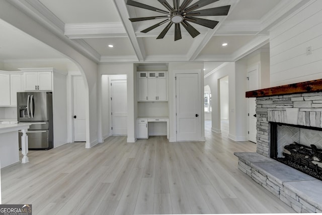 living room with beamed ceiling, a stone fireplace, coffered ceiling, and light wood-type flooring