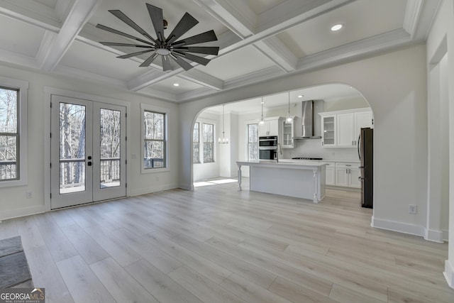 unfurnished living room featuring coffered ceiling, light hardwood / wood-style floors, french doors, and beamed ceiling