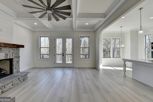 unfurnished living room with crown molding, beam ceiling, a fireplace, french doors, and light wood-type flooring