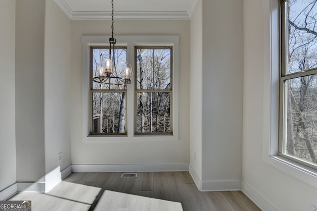 unfurnished dining area featuring an inviting chandelier, ornamental molding, and light wood-type flooring