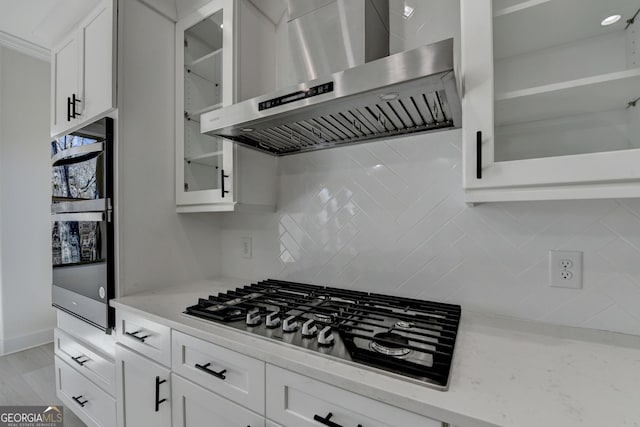 kitchen featuring white cabinetry, appliances with stainless steel finishes, light stone countertops, decorative backsplash, and exhaust hood