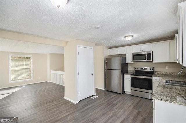 kitchen with appliances with stainless steel finishes, dark hardwood / wood-style flooring, a textured ceiling, white cabinets, and sink