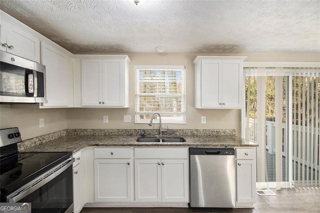 kitchen featuring a textured ceiling, appliances with stainless steel finishes, white cabinetry, dark stone counters, and sink