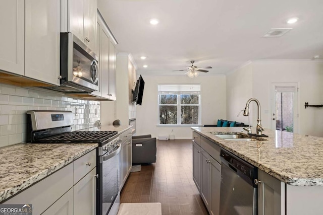 kitchen featuring an island with sink, stainless steel appliances, light stone countertops, ornamental molding, and sink