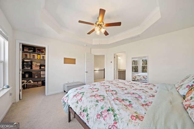 bedroom with ceiling fan, light carpet, a tray ceiling, and connected bathroom