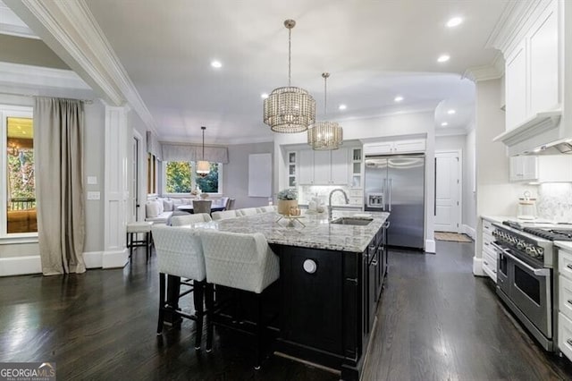 kitchen with pendant lighting, sink, high end appliances, a kitchen island with sink, and white cabinets