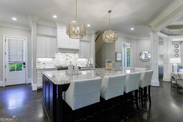 kitchen with backsplash, a large island with sink, pendant lighting, ornamental molding, and white cabinets