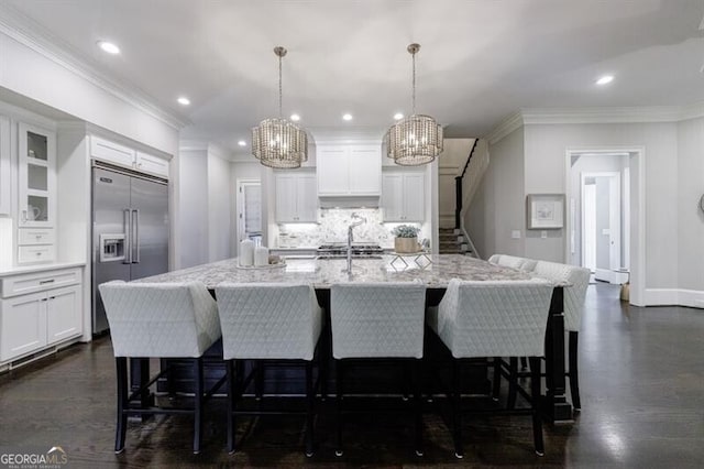 kitchen with hanging light fixtures, an island with sink, stainless steel built in refrigerator, and white cabinets