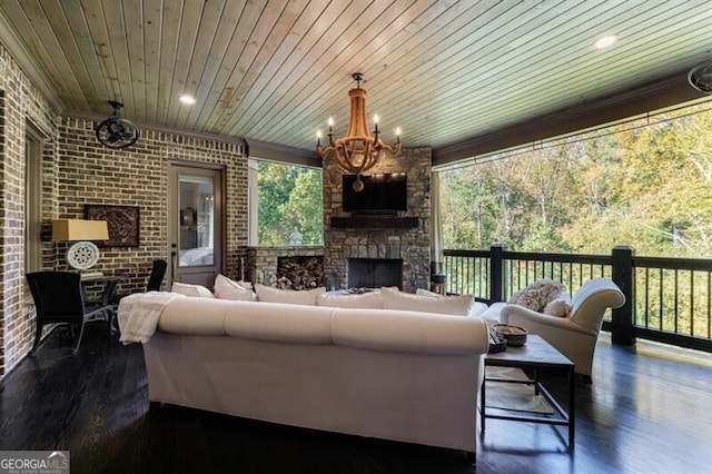 living room with brick wall, an outdoor stone fireplace, wood ceiling, dark hardwood / wood-style flooring, and an inviting chandelier