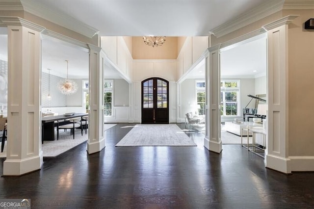 foyer with decorative columns, a notable chandelier, dark wood-type flooring, french doors, and crown molding