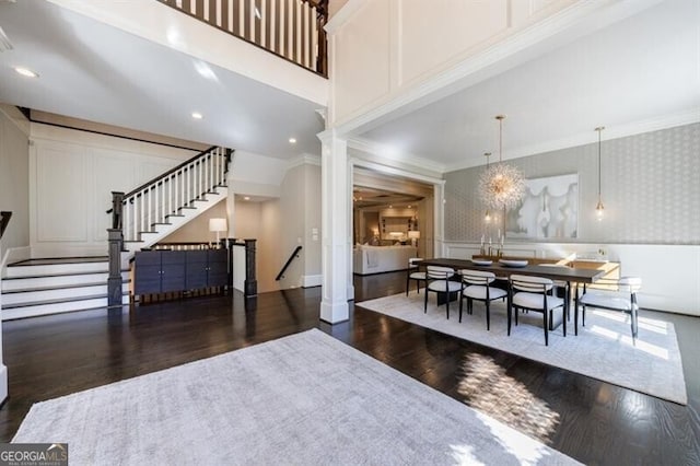 dining space with dark wood-type flooring, ornamental molding, ornate columns, and a towering ceiling