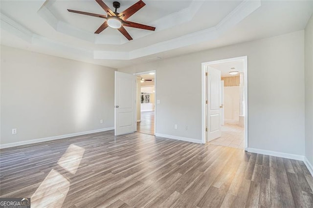 empty room featuring ceiling fan, ornamental molding, dark hardwood / wood-style floors, and a tray ceiling