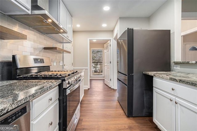 kitchen featuring light wood-type flooring, appliances with stainless steel finishes, white cabinets, wall chimney exhaust hood, and light stone counters