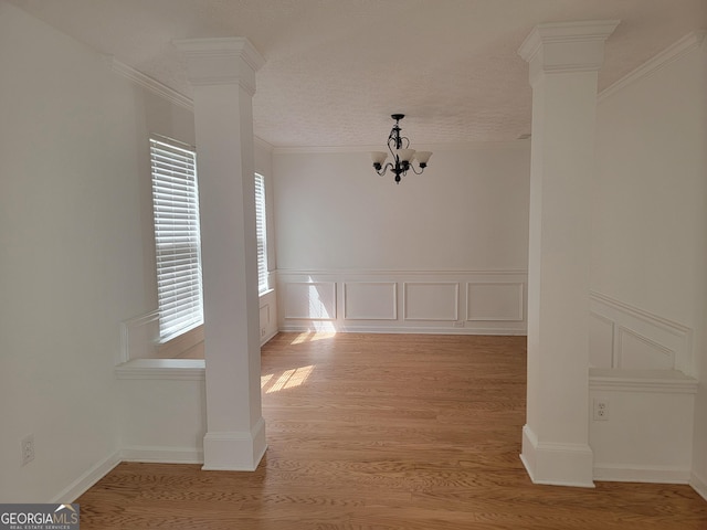 unfurnished dining area featuring a textured ceiling, ornate columns, light hardwood / wood-style floors, ornamental molding, and a notable chandelier