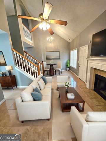 living room with a tiled fireplace, ceiling fan, light tile patterned floors, and high vaulted ceiling