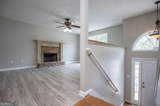 entrance foyer with ceiling fan, a stone fireplace, a textured ceiling, and light hardwood / wood-style flooring