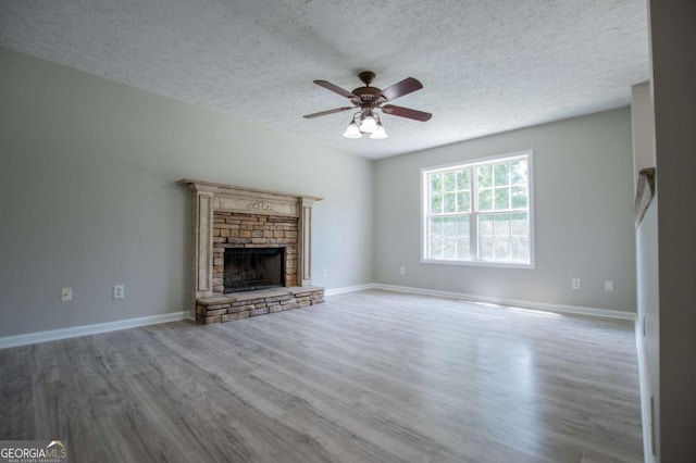 unfurnished living room featuring ceiling fan, light wood-type flooring, a stone fireplace, and a textured ceiling