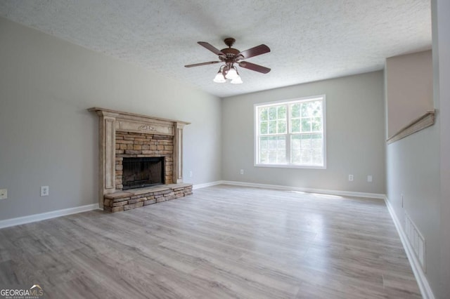 unfurnished living room with a textured ceiling, ceiling fan, light hardwood / wood-style floors, and a stone fireplace