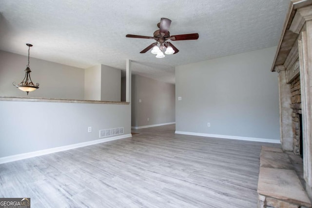 unfurnished living room featuring a textured ceiling, ceiling fan, a fireplace, and light hardwood / wood-style flooring