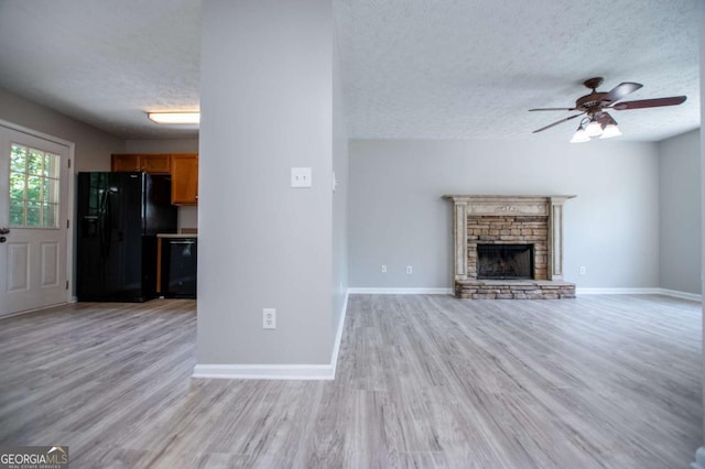 unfurnished living room featuring light hardwood / wood-style floors, ceiling fan, a textured ceiling, and a stone fireplace