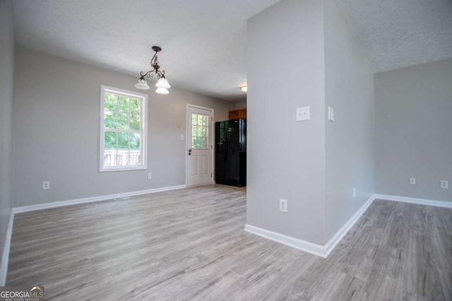 empty room featuring light wood-type flooring, an inviting chandelier, and a textured ceiling