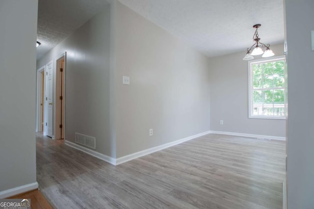 unfurnished room with hardwood / wood-style flooring, a textured ceiling, and a chandelier