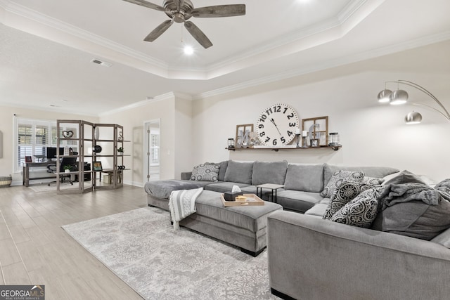 living room with ceiling fan, a tray ceiling, ornamental molding, and light hardwood / wood-style floors