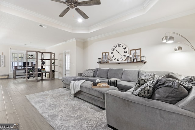 living room with a raised ceiling, ceiling fan, crown molding, and hardwood / wood-style floors