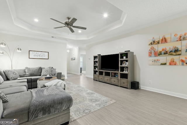 living room with light wood-type flooring, ornamental molding, and a raised ceiling