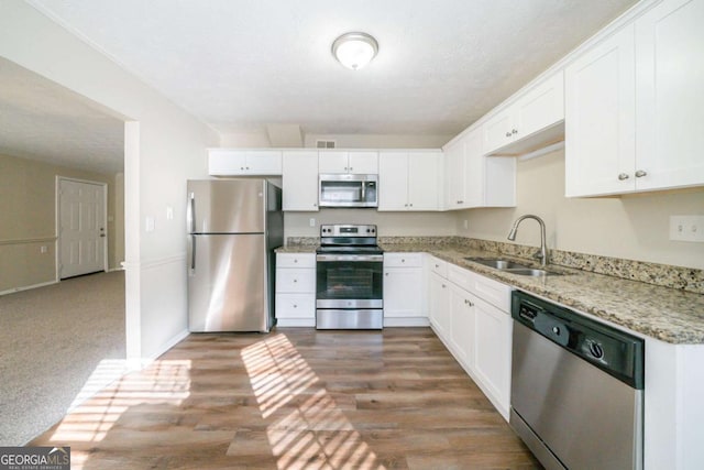 kitchen featuring appliances with stainless steel finishes, dark wood-type flooring, white cabinets, light stone counters, and sink