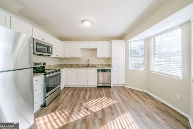 kitchen featuring stainless steel appliances, white cabinets, light hardwood / wood-style flooring, light stone counters, and sink