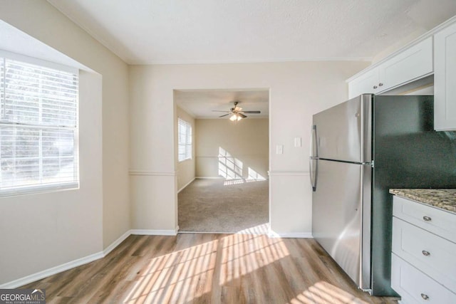 kitchen featuring light stone countertops, white cabinetry, light hardwood / wood-style flooring, and stainless steel refrigerator